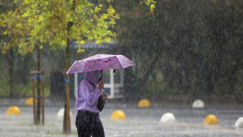 femeie cu masca merge pe strada cu umbrela deschisa in timp ce ploua puternic