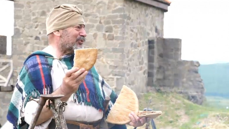 Un bărbat imbracat ca in antichitate vorbeste si arata o paine asa cum mancau soldatii romani