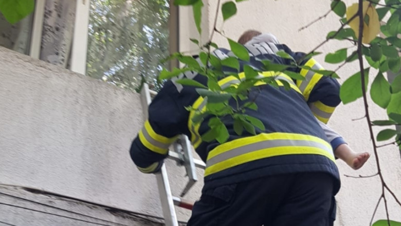 Un pompier salvează un copil aflat pe pervazul unui geam.