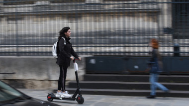 O femeie merge cu trotineta electrică pe un trotuar din Paris.