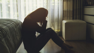 femeie deprimata sta jos langa pat cu fata in palme