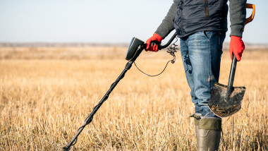 vanator de comori care cauta pe un camp cu un detector de metale si o lopata in mana