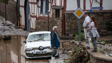 3 oameni stau de vorba langa o masina distrusa de inundatii in germania, apa pe strazi