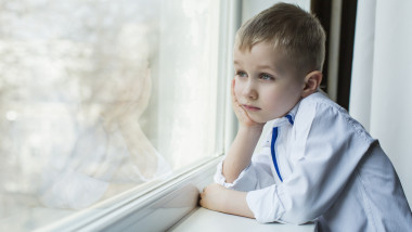 copil care se uita pe fereastra trist