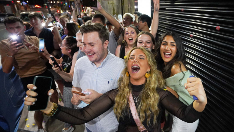 Mai mulți tineri se bucură în fața unui bar din orașul Leeds, după ce restricțiile pandemice au fost ridicate în Anglia la miezul nopții.