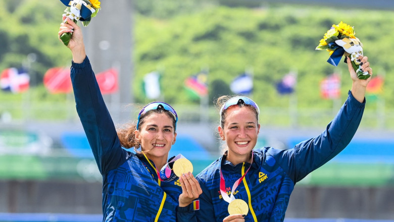 Ancuța Bodnar și Simona Radiș cu medaliile de aur in mana pe podium si buchetul de flori ridicat cu cealalta mana