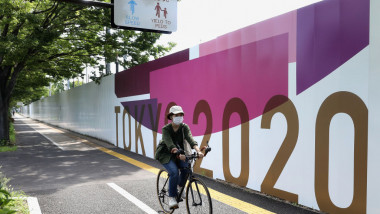 biciclist in tokyo care trece pe langa un banner cu jocurile olimpice