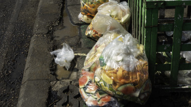 Deșeuri alimentare în pungi de plastic lăsate lângă coșul de gunoi.