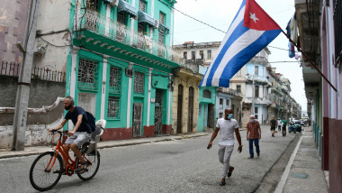 oameni cu măști pe o stradă din Havana. Un steag al Cubei flutură deasupra