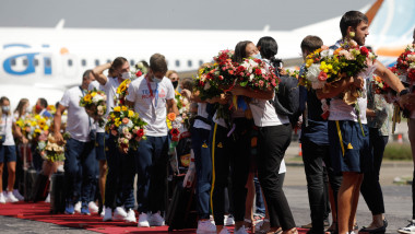 sportivi cu buchete de flori in mana sunt imbratisati pe covorul rosu tras de la avion