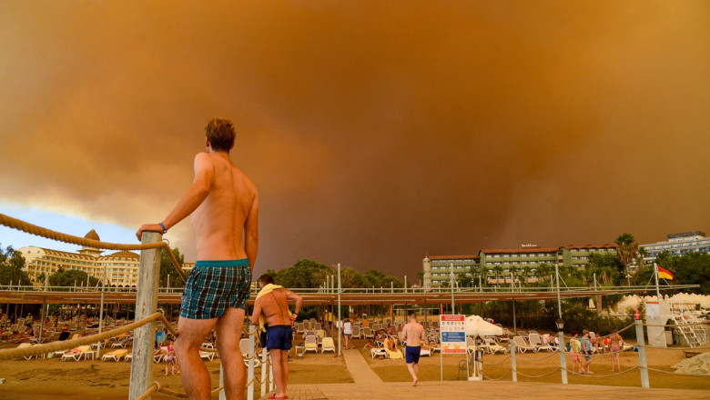 Bărbat în slip pe un teren de tenis privește în depărtare spre un nor de fum provocat de un incendiu