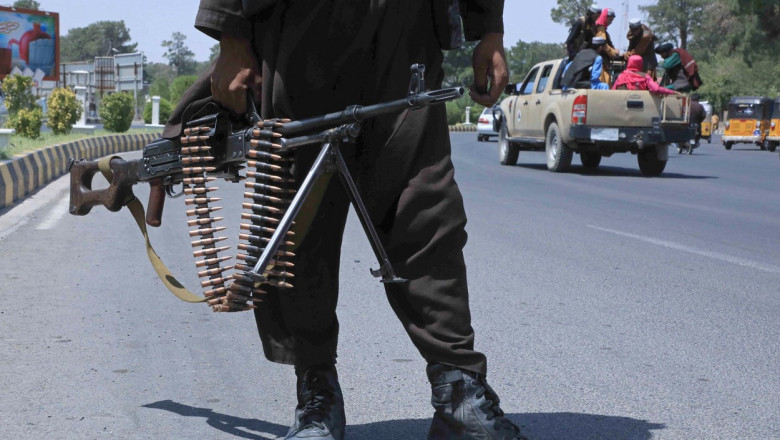 luptator taliban cu o arma in mana pe o sosea in timp ce in fundal se vede o masina pickup cu afgani in spate