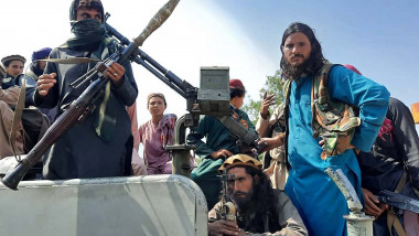 Taliban fighters sit over a vehicle on a street in Laghman