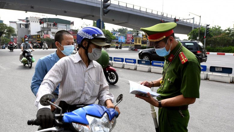 Un polițistul verifică documentele unor șoferi de scuter în timp ce guvernul vietnamez impune noi restricții pandemice pentru a opri răspândirea virusului SARS-CoV-2