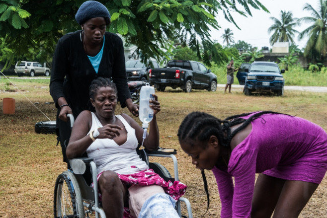 Femeie într-un cărucior cu rotile cu o perfuzie în mână în timpul dezastrului produs de cutremurul din Haiti din 2021