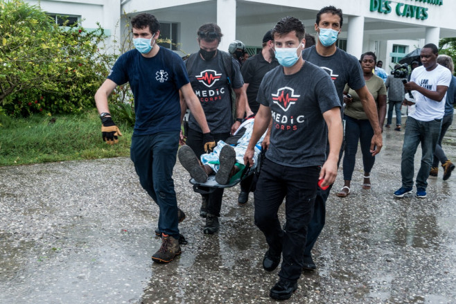 Bărbați în tricouri negre cară un rănit după cutremurul din Haiti