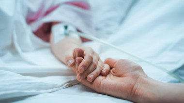 Un copil aflat pe patul de spital este ținut de mână de mama sa.