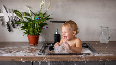 Cute happy baby girl with playing with water and foam in a kitchen sink at home