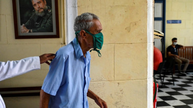Bărbat în vârst merge pe un coridor cu portretrul dictatorului cubanez Fidel Castro