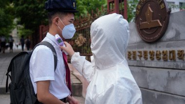 Tânăr nord-coreean căruia i se ia temperatura de către un oficial sanitar în costum de protecție
