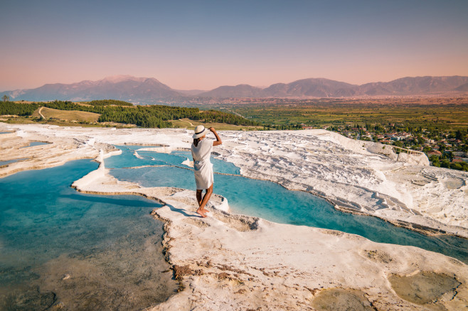 Turkey, Natural travertine pools and terraces in Pamukkale. Cotton castle in southwestern Turkey, girl in white dress with hat natural pool Pamukkale