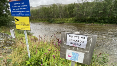 panou improzivat pe malul norvegian al unui rau care avertizează in engleză că este interzisă urinarea in directia rusiei