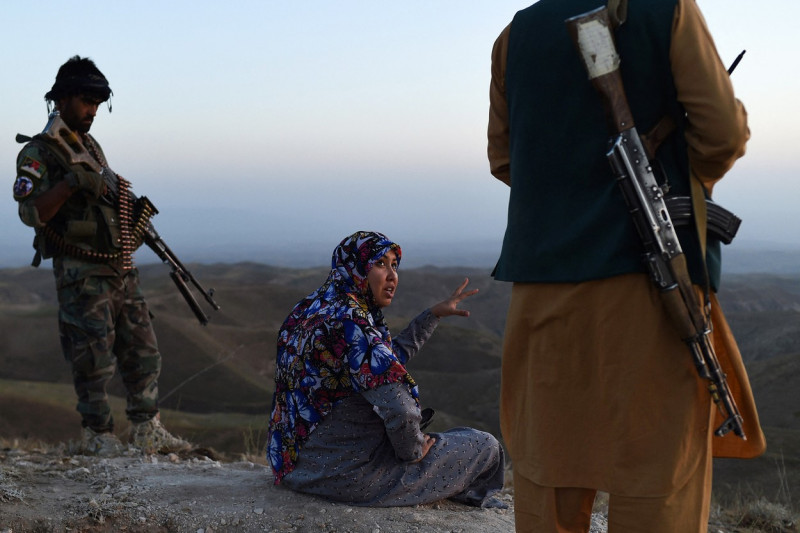 O femeie cu capul acoperit vorbește cu bărbați înarmați
