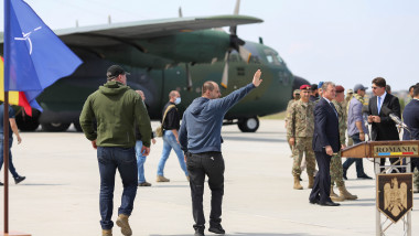 un barbat face cu mana pe aeroport langa un avion militar