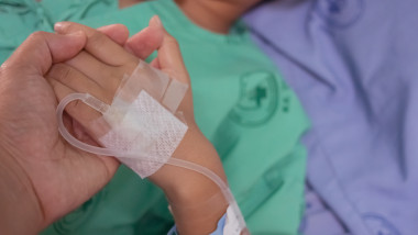 copil cu perfuzie tinut de mana pe patul de spital