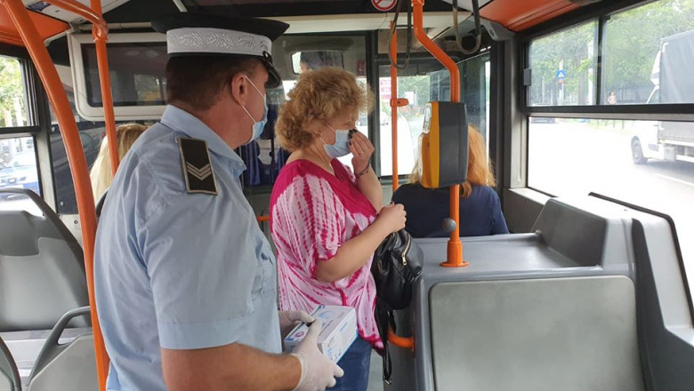 politist cu o cutie de masti in mana langa un pasager dintr-un autobuz