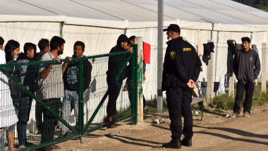 un agent de securitate privește în spatele unui gard la refugiați