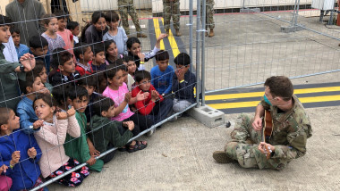 Air Force airman plays the ukulele for Afghan children to keep them entertained at Ramstein Air Base August 24, 2021