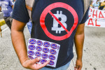 Bărbat cu tricou negru pe care e inscripționat simbolul bitcoin și semnul de interzis la protestele anti-bitcoin din El Salvador