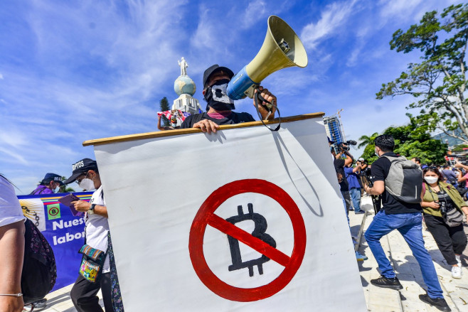 Un bărbat cu un megafon și un banner alb anti-bitcoin