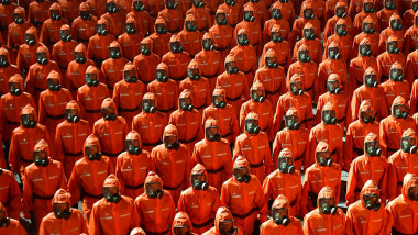 Sute de oameni aliniați, îmbrăcați în costume de protecție la o paradă militară a coreei de nord
