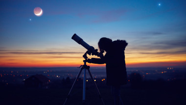 tanara care se uita prin telescop seara la luna si cerul cu stele