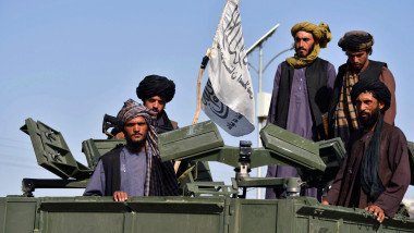 Talibani cu un steag al emiratului islamic al Afganistanului pe un vehicul militar blindat