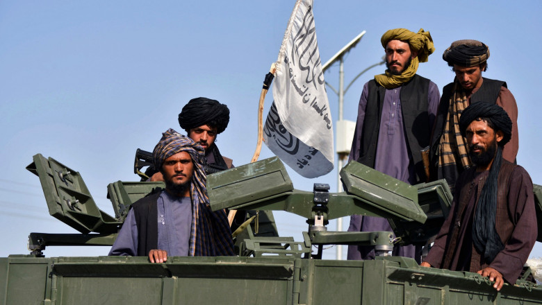 Talibani cu un steag al emiratului islamic al Afganistanului pe un vehicul militar blindat