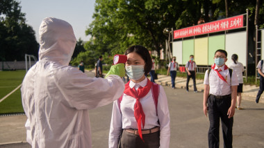 Un lucrător sanitar nord-coreean, în costum de protecție complet, ia temperatura unei eleve în Phenian