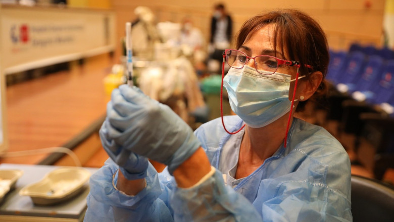 asistenta cu masca si ochelari pregateste o serigă cu vaccin