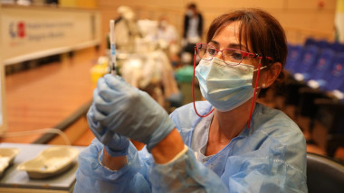 asistenta cu masca si ochelari pregateste o serigă cu vaccin