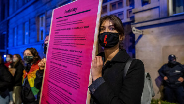 O femeie care ține în mână o pancartă cu mai multe mesaje și poartă o mască neagră de protecție cu fulger roșu pe mijloc, un simbol al protestelor împotriva înăspririi legii avortului din Polonia, participă la un protest pentru libertatea de alegere în fața Ministerului Educației din Varșovia