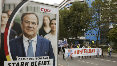 Câțiva protestatari din Berlin trec în marș pe lângă un afiș electoral al lui Armin Laschet.