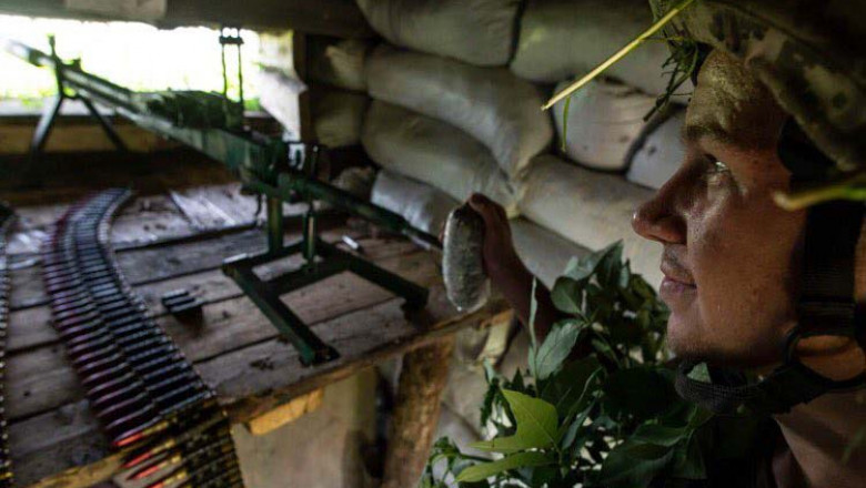 soldat ucrainean cu casca, mitraleria si munitie ascuns in adapost