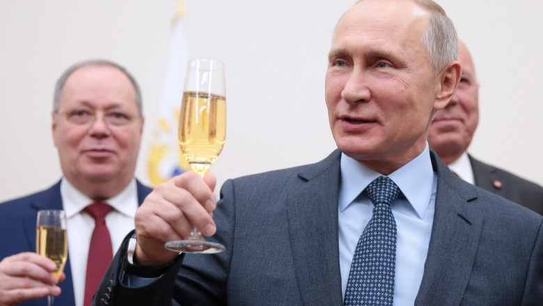 Vladimir Putin zâmbește cu un pahar de șampanie în mână