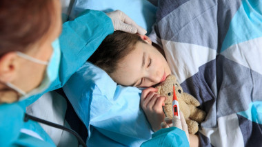 copil care doarme cu ursuletul si caruia i se ia temperatura