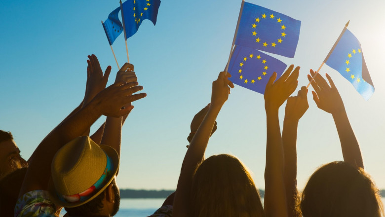 Imagine sugestivă cu mai mulți tineri care țin în mână steagul Uniunii Europene