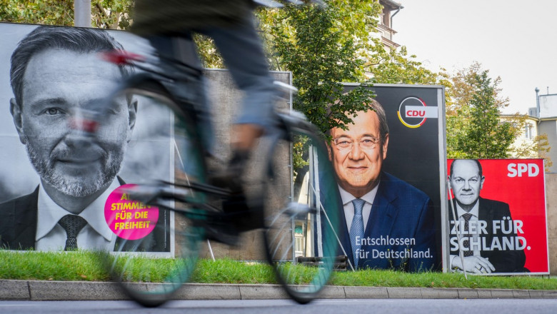 om pe bicicletă merge pe o stradă pe marginea căreia se află afișe cu candidații pentru cancelar la alegerile din germania