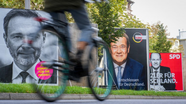 om pe bicicletă merge pe o stradă pe marginea căreia se află afișe cu candidații pentru cancelar la alegerile din germania