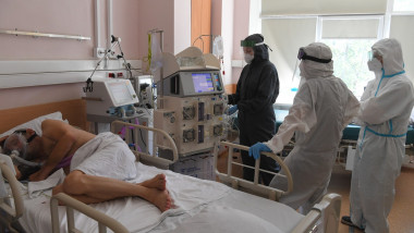 pacient de coronavirus cu mască pe pat și medici care îl îngrijesc